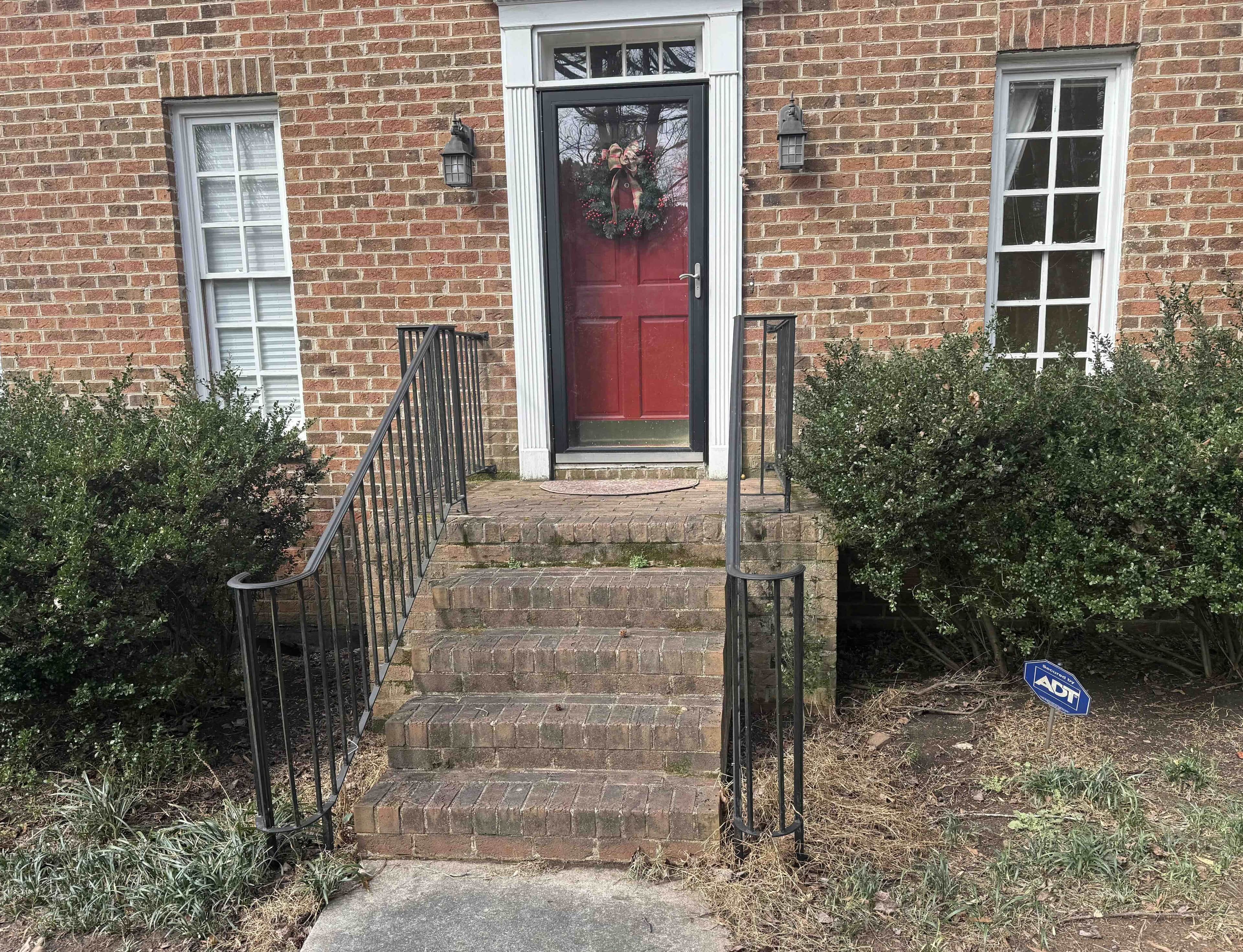 a picture of a Wake Forest brick home with a red door, the steps and sidewalk need to be cleaned